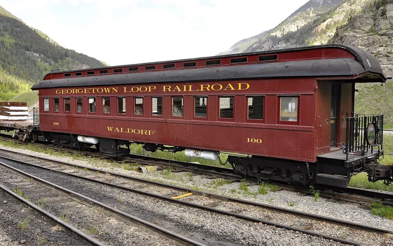 The maroon Georgetown Loop Railroad coach Waldorf, No. 100, on a siding below the mountains, in June 2019