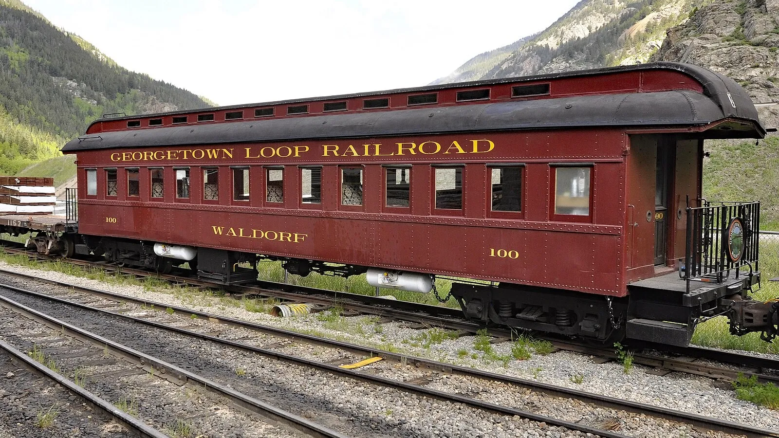 The maroon Georgetown Loop Railroad coach Waldorf, No. 100, on a siding below the mountains, in June 2019